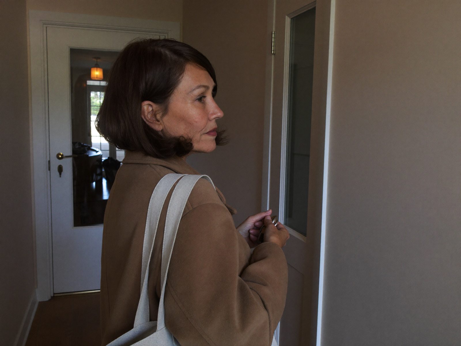 Frau steht früh am Morgen im Mantel im Flur und schaut zur Haustür, bereit zum Aufbruch