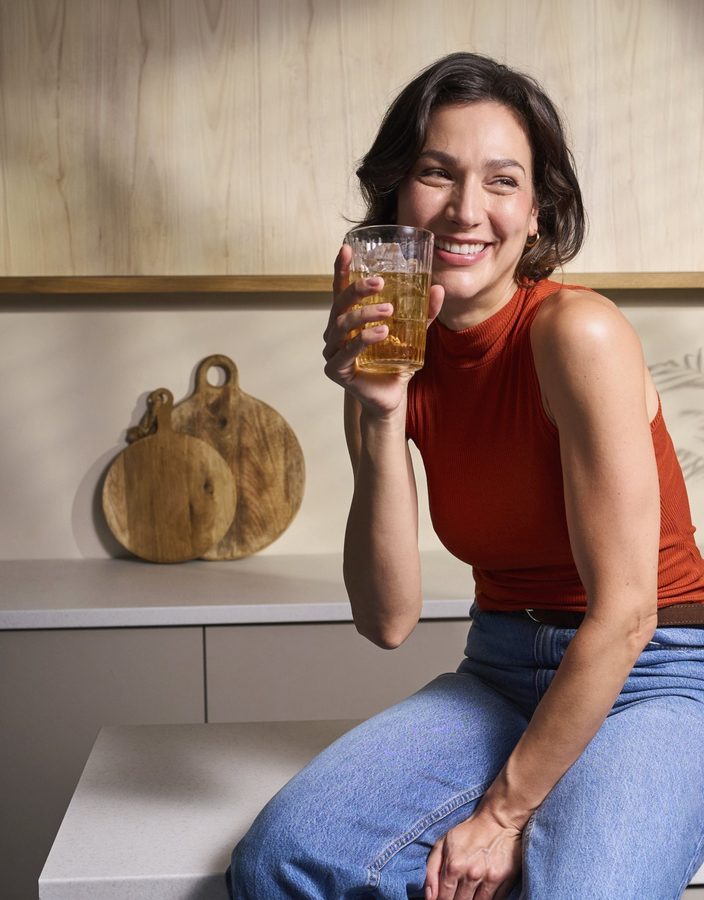 Femme riant le matin dans sa cuisine, un verre à la main, pleine d'énergie