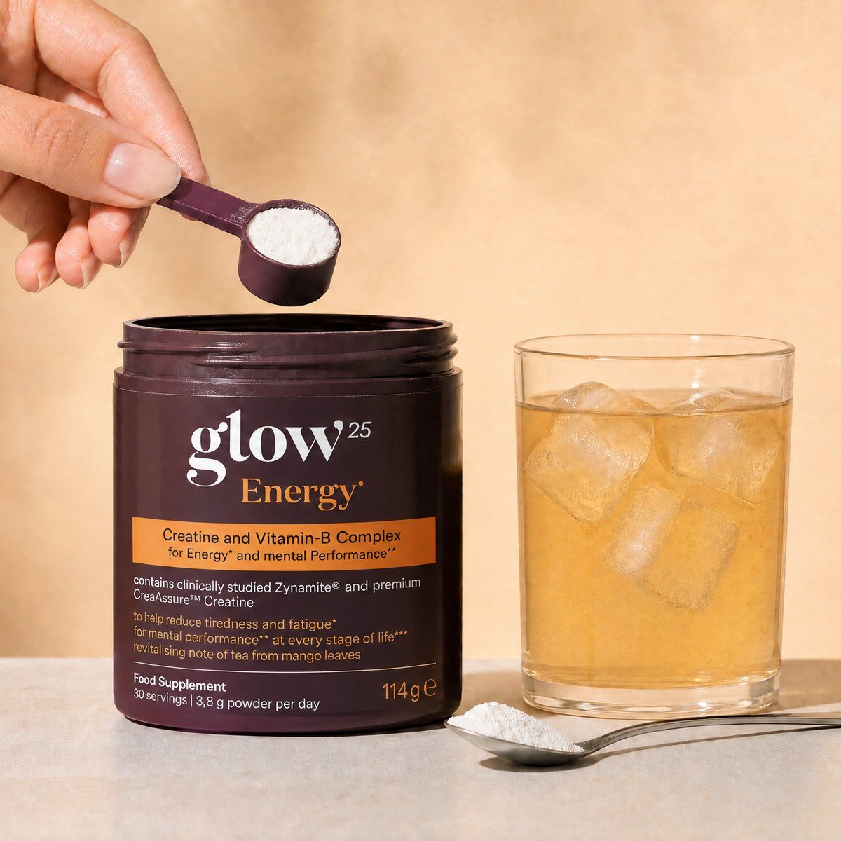 Une main sort la cuillère doseuse du pot Glow25 Energy, à côté une cuillère de poudre et un verre de boisson glacée
