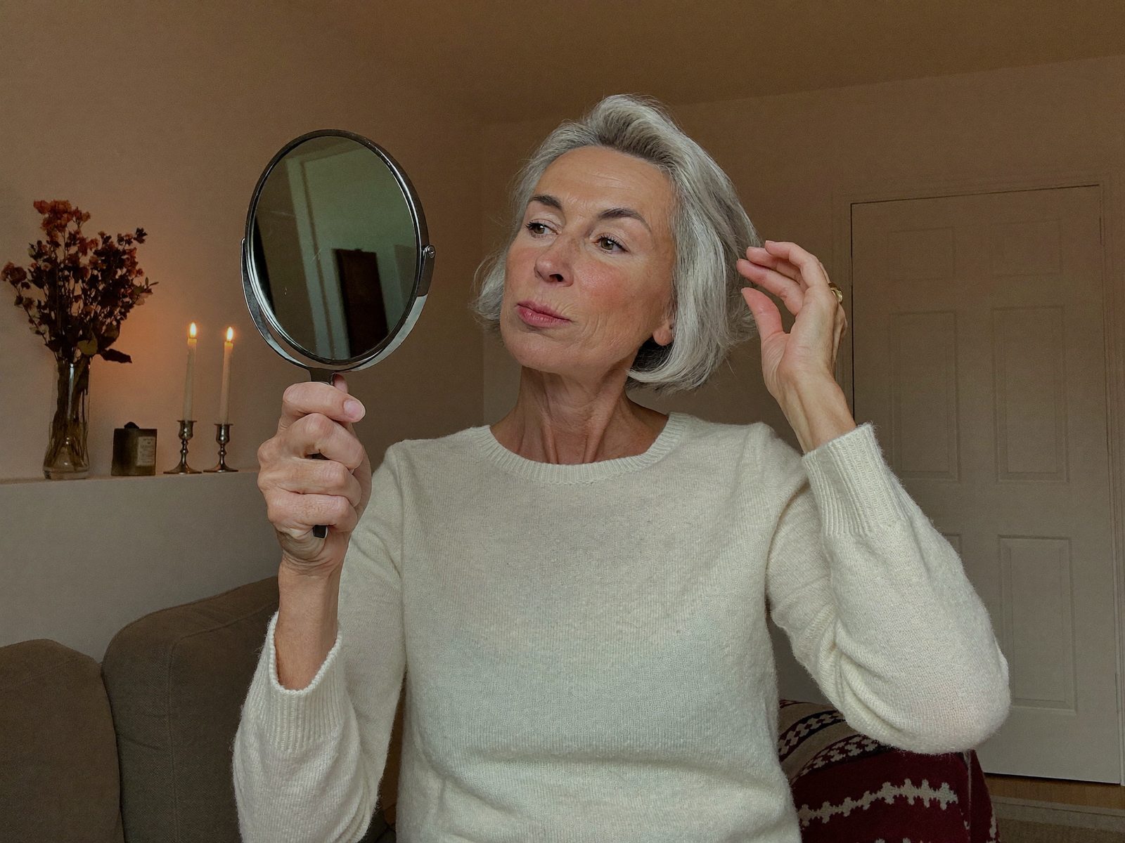 Donna che osserva con occhio critico la pelle e i capelli in uno specchio a mano